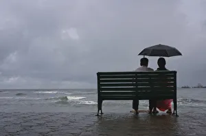 A couple rests on a seaside promenade during a rain shower in Kochi A couple rests on a seaside promenade during a rain shower in Kochi