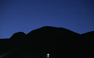 A large crucifix is illuminated below the mountains as the sun sets in the Peloponnese A large crucifix is illuminated below the mountains as the sun sets in the Peloponnese