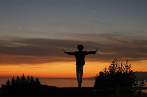 A man balances on a fence post as he watches the sun set over the Pacific Ocean in Santa A man balances on a fence post as he watches the sun set over the Pacific Ocean in Santa
