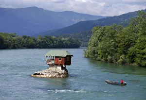 A man powers a boat near a house built on a rock on the river Drina near the western A man powers a boat near a house built on a rock on the river Drina near the western