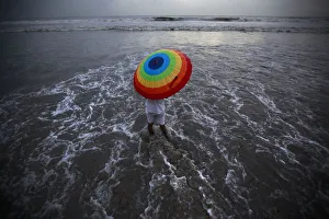 A man takes cover from rain under an umbrella along the shores of the Arabian Sea A man takes cover from rain under an umbrella along the shores of the Arabian Sea