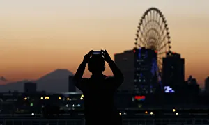 A man takes a picture of a ferris wheel and Mount Fuji during sunset in Tokyo A man takes a picture of a ferris wheel and Mount Fuji during sunset in Tokyo