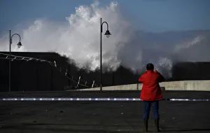 A man takes pictures of waves as they crash against a the port town of Puerto de Vega A man takes pictures of waves as they crash against a the port town of Puerto de Vega