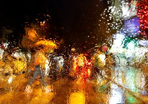 A man with an umbrella is seen through a car window covered with raindrops as he walks A man with an umbrella is seen through a car window covered with raindrops as he walks
