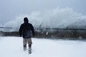 A man watches as ocean waves overtop the seawall during a winter snow storm in the Boston A man watches as ocean waves overtop the seawall during a winter snow storm in the Boston