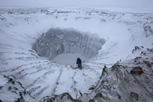 A member of an expedition group stands on the edge of a newly formed crater on the Yamal A member of an expedition group stands on the edge of a newly formed crater on the Yamal