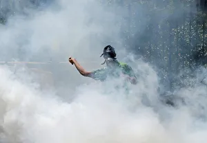 Palestinian protester hurls stones towards Israeli troops as he reacts to tear gas during Palestinian protester hurls stones towards Israeli troops as he reacts to tear gas during