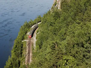 A passenger train moves along a railway along the bank of the Yenisei River near the A passenger train moves along a railway along the bank of the Yenisei River near the