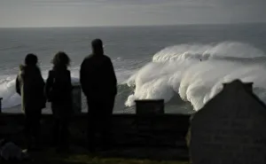 People look at waves as they crash against a lighthouse in the port town of Tapia de People look at waves as they crash against a lighthouse in the port town of Tapia de