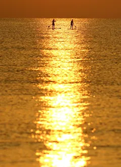 People paddle on a stand-up board during sunrise in a beach in Larnaca People paddle on a stand-up board during sunrise in a beach in Larnaca