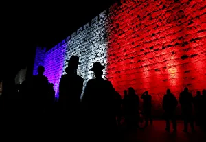 People walk past the walls of Jerusalems Old City lit in blue, white and red People walk past the walls of Jerusalems Old City lit in blue, white and red