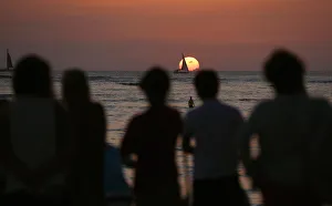 People watch a boat sail in front of the setting sun on New Years Eve on Waikiki Beach People watch a boat sail in front of the setting sun on New Years Eve on Waikiki Beach