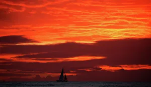 A sailboat passes in front of clouds lit up by the sunset sky off Waikiki in Hawaii, U.S A sailboat passes in front of clouds lit up by the sunset sky off Waikiki in Hawaii, U.S
