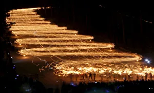 Spectators watch hundreds of skiers descend from a slope while holding lit torches in the Spectators watch hundreds of skiers descend from a slope while holding lit torches in the