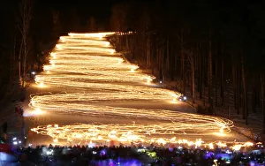 Spectators watch skiers descending down from the slope while holding lit torches in the Spectators watch skiers descending down from the slope while holding lit torches in the
