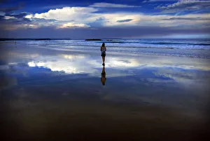 Storm clouds and dust can be seen in the sky above a woman as she walks at dusk along Storm clouds and dust can be seen in the sky above a woman as she walks at dusk along