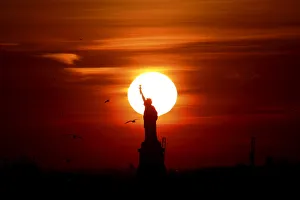 The sun sets behind the Statue of Liberty in New Yorks Harbor as seen from the Brooklyn The sun sets behind the Statue of Liberty in New Yorks Harbor as seen from the Brooklyn