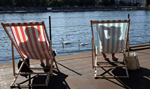 Swans swim on the Vltava River as people sunbathe on deck chairs during a heat wave Swans swim on the Vltava River as people sunbathe on deck chairs during a heat wave