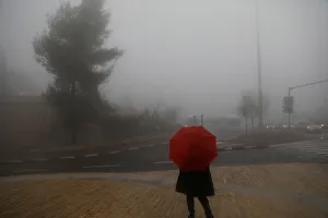 A woman holds an umbrella as she stands on the sidewalk during a foggy day in Jerusalem A woman holds an umbrella as she stands on the sidewalk during a foggy day in Jerusalem