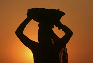 A woman labourer carrying cement is silhouetted against the setting sun at the site of a A woman labourer carrying cement is silhouetted against the setting sun at the site of a