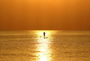 A woman paddles on a stand-up board during sunrise in a beach in Larnaca A woman paddles on a stand-up board during sunrise in a beach in Larnaca