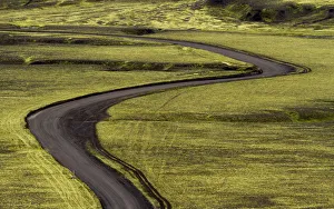 Europe, Iceland. Black dirt road curves through green countryside Europe, Iceland. Black dirt road curves through green countryside