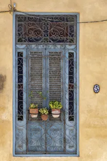 Three flower pots sit in wrought iron gate in front of blue door in Old Havana Three flower pots sit in wrought iron gate in front of blue door in Old Havana