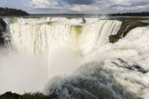 The headwater of Iguazu Falls with a rainbow from the Argentinian side with Brazil in the background The headwater of Iguazu Falls with a rainbow from the Argentinian side with Brazil in the background
