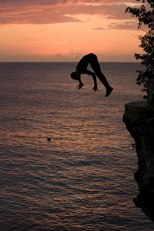 Jamaica, Negril, Silhouette of young man leaping from from cliff above Pirates Cave Jamaica, Negril, Silhouette of young man leaping from from cliff above Pirates Cave