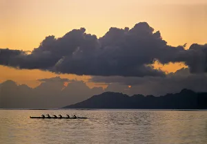An outrigger canoe team practices off the coast of the island of Tahiti as the sun An outrigger canoe team practices off the coast of the island of Tahiti as the sun
