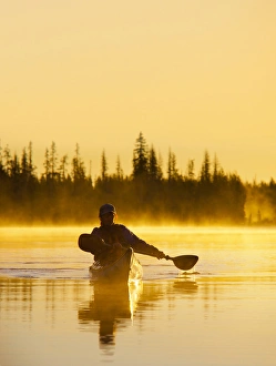 USA, Oregon. A woman in a sea kayak paddles at dawn on Big Lake, Oregon, in the Oregon Cascades USA, Oregon. A woman in a sea kayak paddles at dawn on Big Lake, Oregon, in the Oregon Cascades