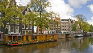 A wooden houseboat with lots of flowers on Prinsengracht Canal with colorful buildings A wooden houseboat with lots of flowers on Prinsengracht Canal with colorful buildings
