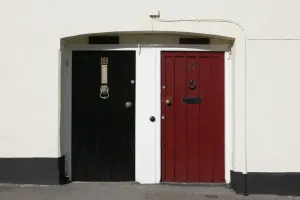 Prints of A pair of front doors painted red and black with the white walls of houses number 24 and 25 in a village on the Rames Head Cornwall on the South Coast of England Rame Prints: Red and Black Doors Print, Cornwall Village Scene