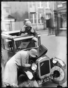 Two women in cloche hats examine a car engine