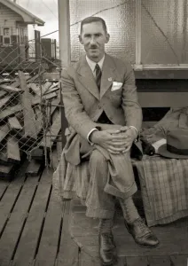 A man sits on a pier, coat and hat beside him