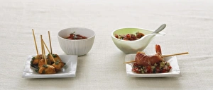 Chicken pieces on skewers on small square plate and bowl of sauce, king prawn on skewer on bed salsa on small square Chicken pieces on skewers on small square plate and bowl of sauce, king prawn on skewer on bed salsa on small square