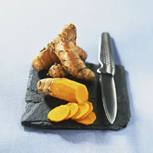 Curcuma longa, two fresh Turmeric rhizomes on slate tile with metal grating knife Curcuma longa, two fresh Turmeric rhizomes on slate tile with metal grating knife