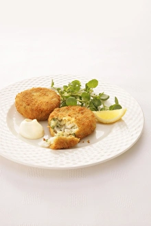 Haddock and herb fishcakes coated in breadcrumbs, served with watercress, slice of lemon and mayonnaise on a plate Haddock and herb fishcakes coated in breadcrumbs, served with watercress, slice of lemon and mayonnaise on a plate