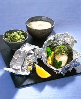 Halibut with fresh herbs and seasoned rice served in foil parcels, with lemon wedges and white sauce in bowl Halibut with fresh herbs and seasoned rice served in foil parcels, with lemon wedges and white sauce in bowl
