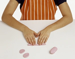 Hand model wearing an orange and white striped apron, making oval shapes from pink fondant icing Hand model wearing an orange and white striped apron, making oval shapes from pink fondant icing
