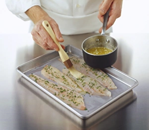 Plaice fillets sprinkled with parsley being brushed with molten butter Plaice fillets sprinkled with parsley being brushed with molten butter
