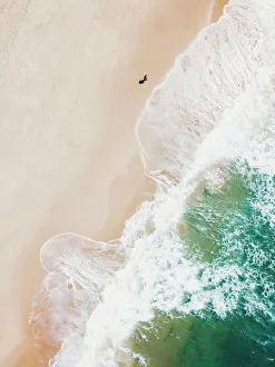 An aerial beach shot of guy walking on the beach and the waves breaking on the shore An aerial beach shot of guy walking on the beach and the waves breaking on the shore