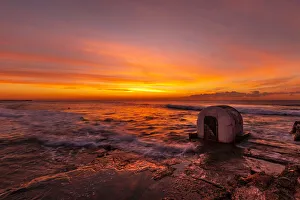 Beautiful red, yellow and orange colors of a sunrise over the ocean with a little concrete hut Beautiful red, yellow and orange colors of a sunrise over the ocean with a little concrete hut
