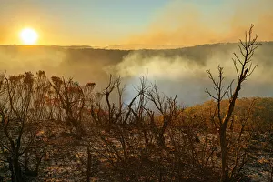 Sun setting in burnt smouldering mountain landscape with smoke filled valley after forest Sun setting in burnt smouldering mountain landscape with smoke filled valley after forest