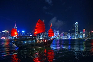 A Traditional Chinese Junk Sailing In Victoria Harbour With View of Hong Kong Island Skyline At Night, Hong Kong, China A Traditional Chinese Junk Sailing In Victoria Harbour With View of Hong Kong Island Skyline At Night, Hong Kong, China