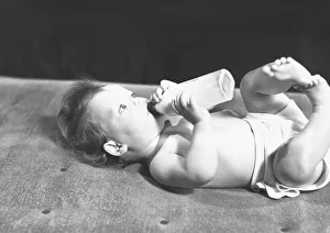 Baby (6-9 months) lying on bed, drinking from bottle, (B&W) Baby (6-9 months) lying on bed, drinking from bottle, (B&W)