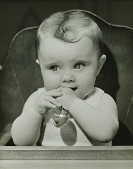 Baby (6-9 months) sitting in high chair, holding spoon, (B&W), portrait Baby (6-9 months) sitting in high chair, holding spoon, (B&W), portrait