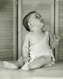 Baby boy (6-12) sitting on floor indoors, looking upwards, (B&W) Baby boy (6-12) sitting on floor indoors, looking upwards, (B&W)