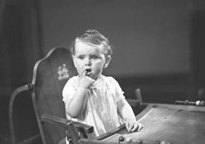 Baby girl (9-12 months) sitting in high chair, holding finger in mouth, (B&W) Baby girl (9-12 months) sitting in high chair, holding finger in mouth, (B&W)