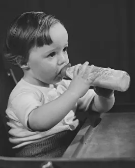 Baby girl (9-12 months) sitting in highchair, drinking milk from bottle (B&W) Baby girl (9-12 months) sitting in highchair, drinking milk from bottle (B&W)